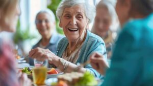 Two older adults chatting together at a table in a well-lit, comfortable communal living area