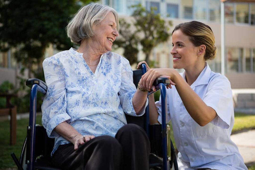 Older residents walk through a bright assisted living hallway with handrails, clear floors, and emergency call buttons.